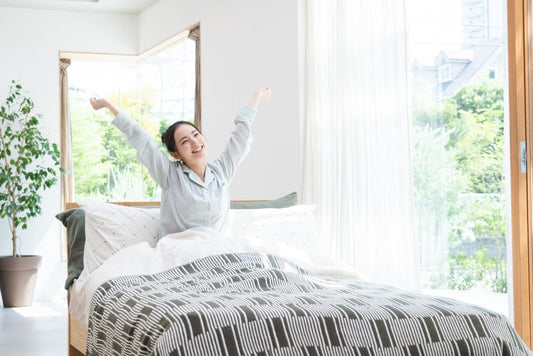  A woman sits comfortably in bed, arms raised, enveloped in a cosy summer duvet.