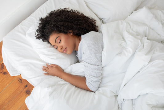 Hispanic woman is lying down on a bed with a white comforter covering her, appearing relaxed and comfortable in a bedroom setting, view above